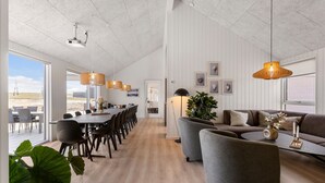 Una habitación amplia con una larga mesa de comedor, varias sillas, un sofá y una planta grande.
