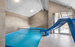 An indoor swimming pool with a blue slide, tiled walls, and a clear glass entrance. - Cozy home in Bogense with sauna (Bogense)