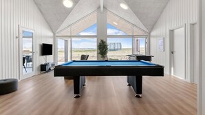 Una mesa de billar en una habitación con ventanas amplias, pisos de madera y un televisor de pantalla plana.