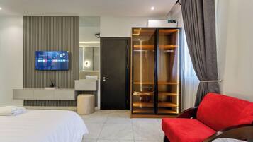 Quarto de hotel moderno com cama, TV fixada na parede, guarda-roupa e uma cadeira vermelha.