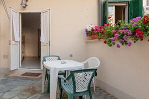 An outdoor seating area with a table and chairs, a potted plant with flowers, and a door leading to an interior space. - Cozy 'Livorno Apartment' with Wi-Fi and Air Conditioning (Livorno)