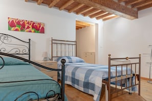A room with two beds, wooden beams on the ceiling, a painting on the wall, and a small table with a lamp. - Cozy 'Livorno Apartment' with Wi-Fi and Air Conditioning (Livorno)