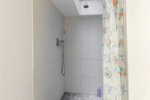Ducha con cabezal de ducha de mano, grifo empotrado en la pared y cortina de baño con estampado floral.