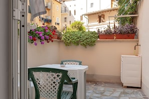 Un pequeño patio exterior con una mesa, sillas, plantas en macetas y un armario blanco.