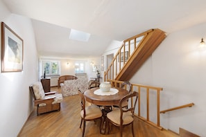 Un coin repas avec une table et des chaises en bois, un escalier avec des rampes en bois, et une vue sur le salon en arrière-plan.