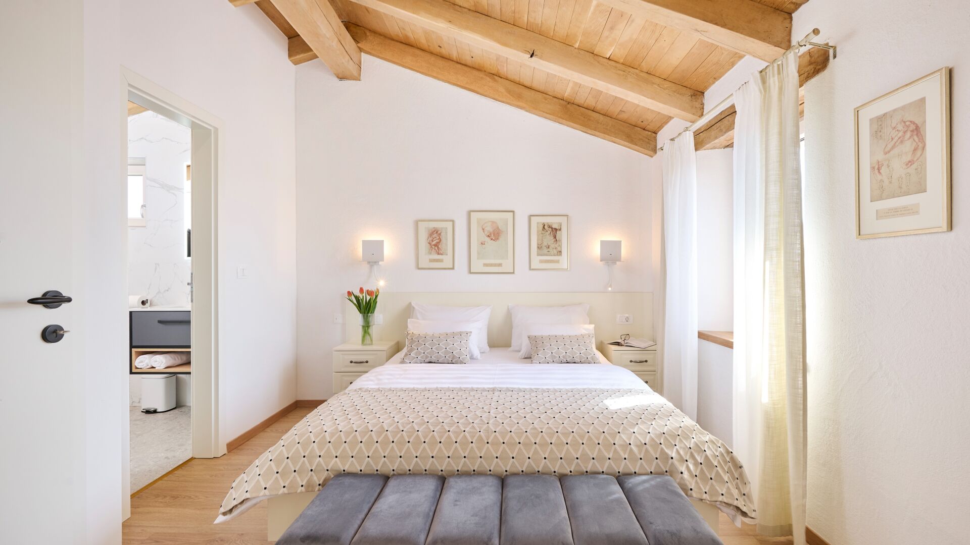 A bedroom with a bed, bedside tables, a bench, a mirror, and framed pictures on the wall.