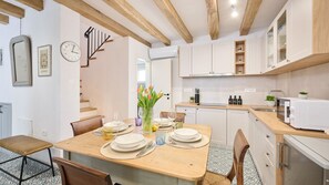 A modern kitchen with white cabinets, a wooden dining table set for four, and a built-in oven. - Casa Pove by Villas Guide (Baredine)