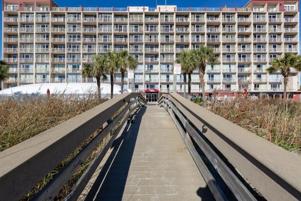 A multi-story hotel with balconies, a central walkway, and palm trees.