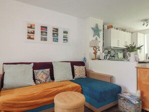 A cozy room with a sofa, ottoman, and a small table with a pitcher and plant. - 140 Atlantic Reach (St. Columb Major)