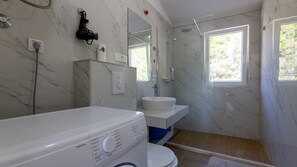 Ein Badezimmer mit Waschmaschine, Waschbecken, Dusche und Spiegel.