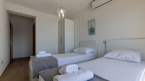 Ein Hotelzimmer mit zwei Einzelbetten, einer grauen Bank, einer weißen Klimaanlage und einem Bild an der Wand.