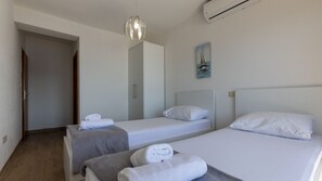 A hotel room with two single beds, a grey bench, a white air conditioning unit, and a painting on the wall. - Apartman Jelinic 2 by Villas Guide (Klek)