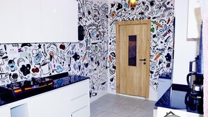 A kitchen with a white countertop, a wooden door, and a wall decorated with food and drink illustrations. - Stan Haven Apartment (Abuja)