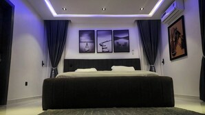 A modern bedroom with a large bed, recessed ceiling lights, and three framed artworks on the wall. - Stan Haven Apartment (Abuja)