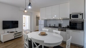 Une cuisine moderne avec des meubles blancs, une table à manger et un téléviseur.