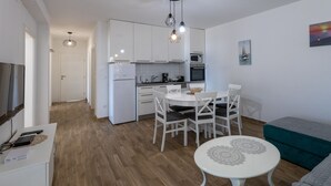 Une cuisine moderne avec des meubles blancs, une table à manger avec des chaises, une petite table ronde ornée d’un chemin de table décoratif et un canapé de couleur turquoise.