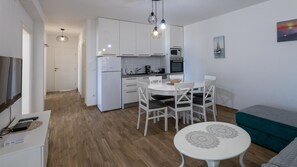 A modern kitchen with white cabinets, a dining table with chairs, a small round table with a decorative doily, and a teal sofa. - Apartman Jelinic 1 by Villas Guide (Klek)