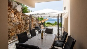 Une terrasse extérieure avec une table, des chaises, un barbecue et une vue sur la mer.