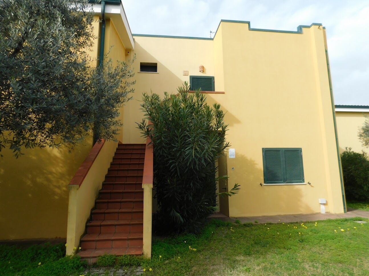 A yellow building with a staircase, a small window, and a door.