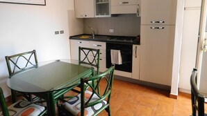 A compact kitchen with white cabinets, a dining table with chairs, and a tiled floor. - Verde Mare Beach Houses (Contrada Taverna)
