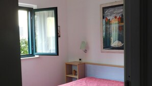 A bedroom with a bed, a window, a shelf, and a painting on the wall. - Verde Mare Beach Houses (Contrada Taverna)