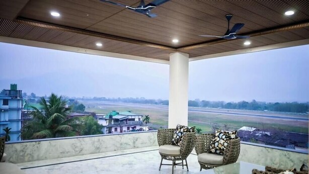 A balcony with two wicker chairs, a marble floor, and a view of a runway and buildings.