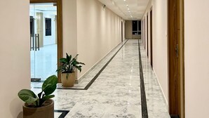 A long, well-lit hallway with marble flooring, potted plants, and wooden doors.