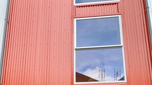 Kaksikerroksinen rakennus, jonka ulkoseinät ovat punaiset, ja jossa on autotalli sekä pieni sisäänkäynti.