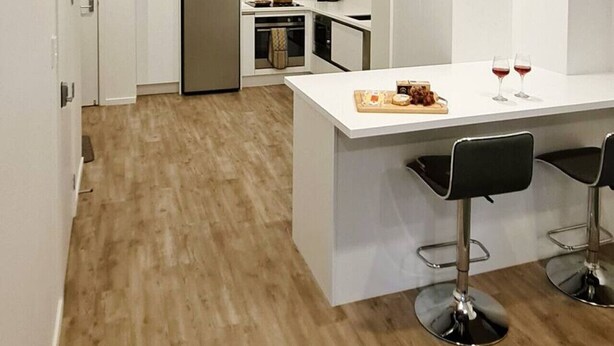 A modern kitchen with white cabinetry, a central island with bar stools, and a stainless steel refrigerator. - Smart Stay: Modern Apt w/ Free Parking, Near Uni (Dunedin)