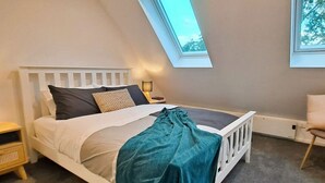 A bedroom with a sloped ceiling, a bed with white headboard, a bedside table, a lamp, and a view through a skylight. - Smart Stay: Modern Apt w/ Free Parking, Near Uni (Dunedin)