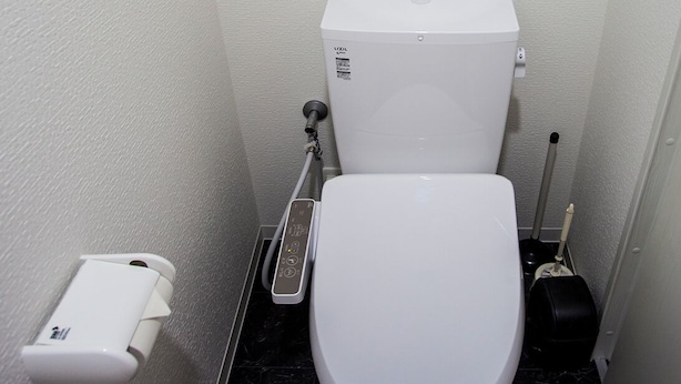 A small, modern bathroom with a white toilet, a hand dryer, and a toilet paper holder. - Ustay nippori (Tokyo)