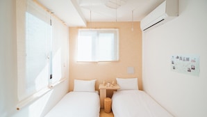 A small, clean room with two single beds, a small table with a basket, and a wall-mounted map. - Ustay nippori (Tokyo)