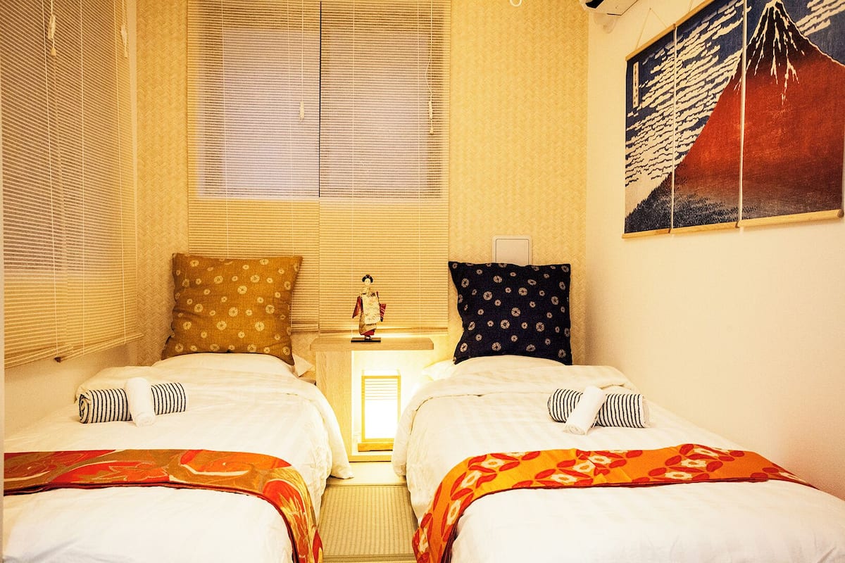 A room with two beds, a nightstand with a lamp, and a wall-mounted painting.
