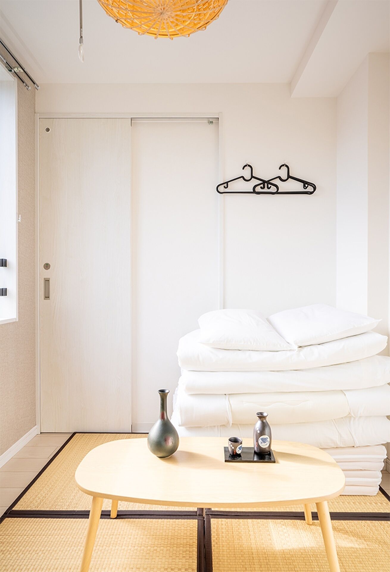A room with a bed, a bedside table with a vase and a cup, a wall-mounted towel rack, and a door.