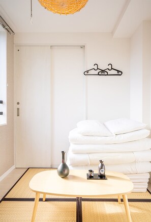 A room with a bed, a bedside table with a vase and a cup, a wall-mounted towel rack, and a door. - Ustay nippori (Tokyo)