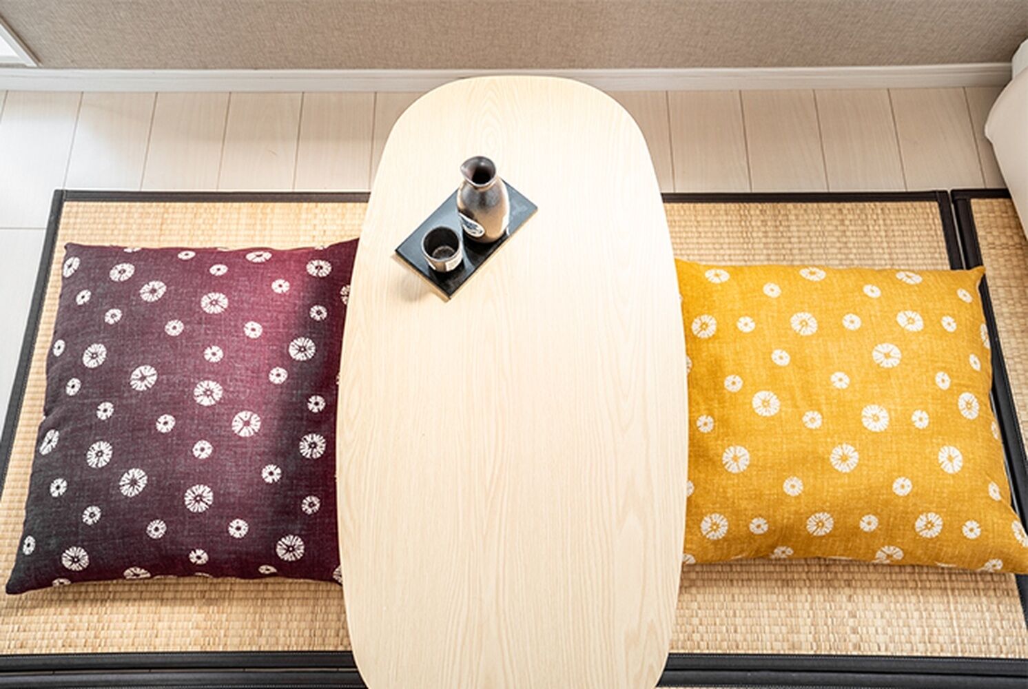 A tatami mat room with a low table and two pillows with floral patterns.