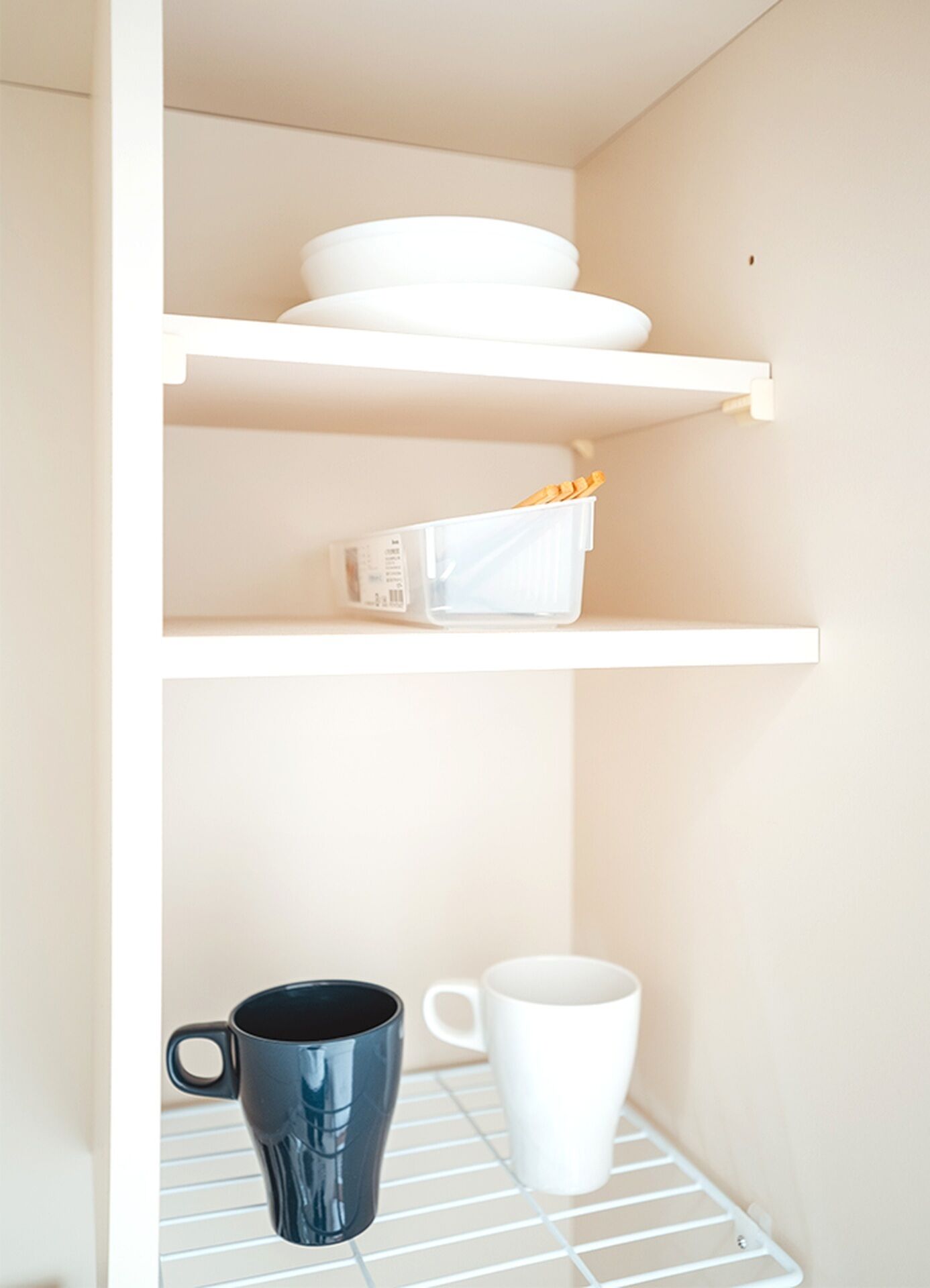 A kitchen shelf with white dishes and a white container.