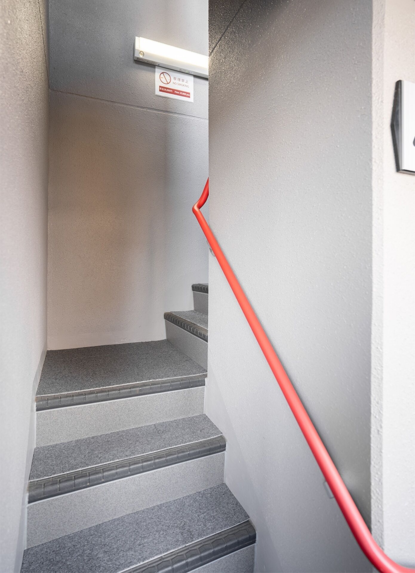 A staircase with a red handrail and a 'No Smoking' sign above it.