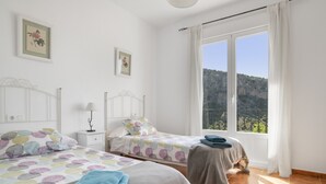 Un dormitorio con dos camas, una mesita de noche, una lámpara y una ventana con vistas a un paisaje montañoso.