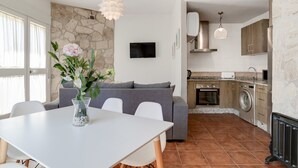 Une cuisine moderne avec un mur en pierre, un coin repas avec une table et des chaises blanches, et un canapé gris.