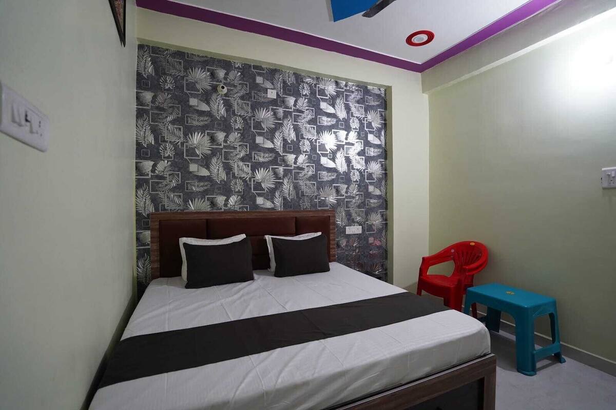A bedroom with a bed, a red chair, a blue stool, and a patterned wall.