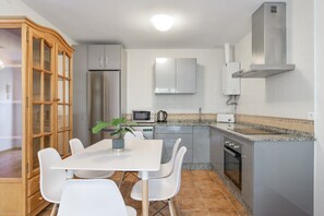 A modern kitchen with a dining table, chairs, a microwave, a refrigerator, and a stove. - Apartment 'Casa Riguelas' with Mountain View, Shared Pool and Shared Garden (Málaga)