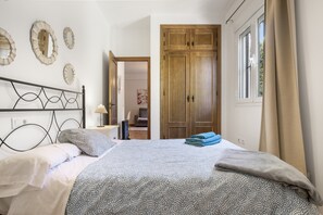 A bedroom with a bed, a wooden wardrobe, and a window with curtains. - Apartment 'Casa Riguelas' with Mountain View, Shared Pool and Shared Garden (Málaga)