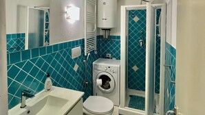 Een kleine badkamer met een wastafel, toilet, wasmachine en douchecabine.