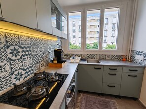 Cozinha compacta com fogão a gás, pia e janela com vista para uma área residencial.