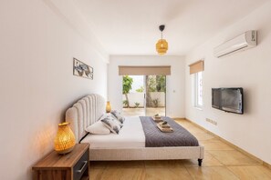 Ein Schlafzimmer mit Bett, Nachttisch, Lampe, Fernseher und Blick ins Freie.