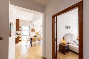 Ein Zimmer mit Bett, Nachttisch und kleinem Tisch mit Lampe. Im Hintergrund ist ein Essbereich mit Tisch und Stühlen zu sehen.