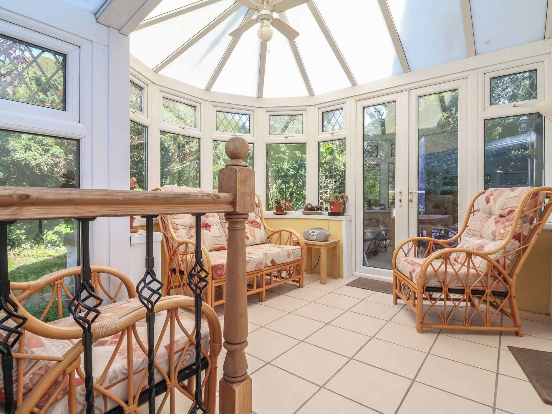 A conservatory with wicker furniture, a wooden table, and a ceiling fan.