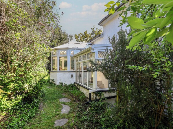 A white house with a glass conservatory, surrounded by greenery. - Honey Cottage (Ilfracombe)