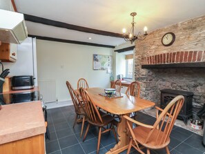 A dining area with a wooden table and chairs, a stone wall, a clock, and a fireplace. - Honey Cottage (Ilfracombe)